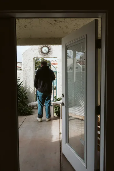 A front door standing wide open onto a walkway, with a person walking out toward an open gate