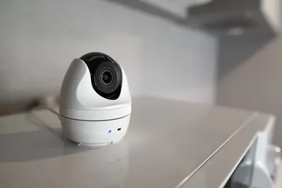 A small white pan and tilt smart camera sitting on a shelf in a bright home interior